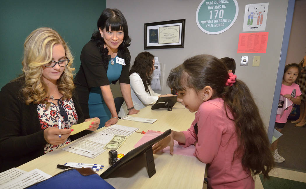 Sonia Anderson, founder and CEO of Andson, Inc., center, and teller Emilee Savage, left, help first-grader Claudia Chaves with a deposit at the Piggy Bank in Howard E. Hollingsworth Elementary Sch ...