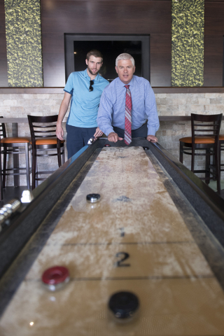 Mark Kelly, vice president of casino operations with Bally's, Paris and Planet Hollywood, right, and his son, Ryan Kelly, pool operations manager at The Linq Hotel, play a game of shuffleboard in  ...