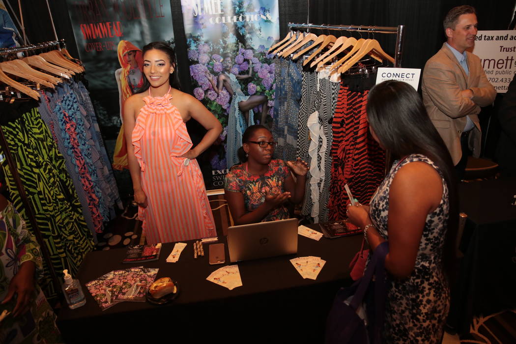 Taylor Odum shows off bathing suit cover-up fashion by Si Mee Collections while Chaize Macklin speaks to a chamber member during the Henderson Chamber of Commerce’s CONNECT Expo+Panel+Mixer even ...