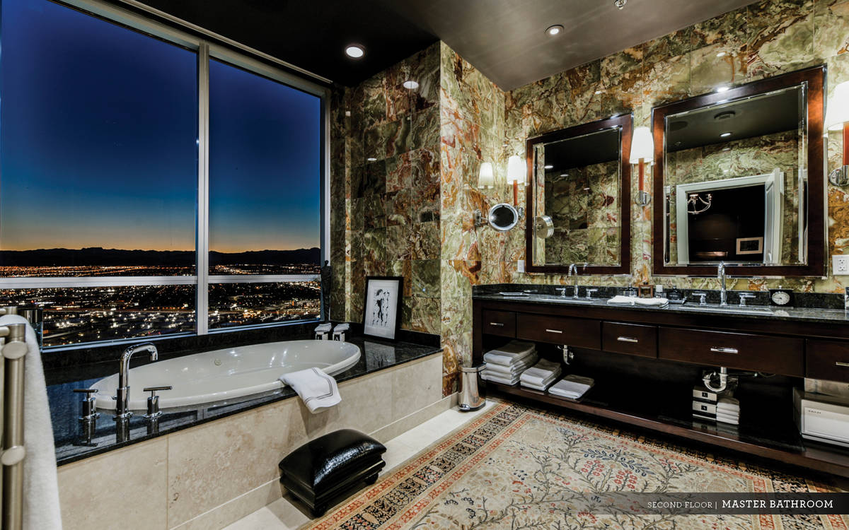 The spa-like master bath showcases multicolored granite-esque stone walls, soaking tub with a v ...