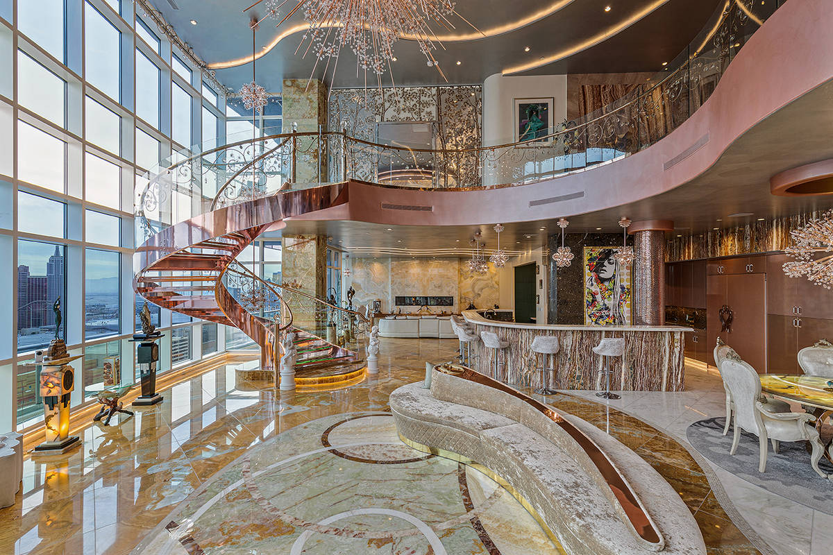 A rose-gold lighted glass and crystal circular floating staircase is the focal point of the gr ...