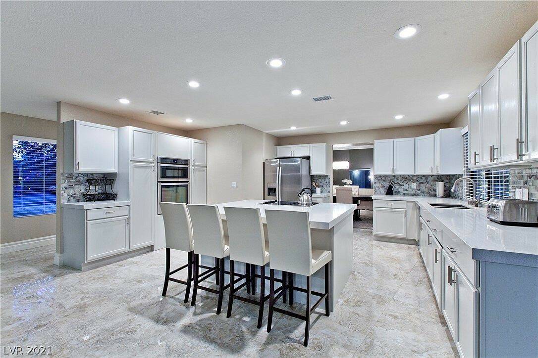 The fully renovated kitchen features custom white cabinetry, an expansive center island with qu ...