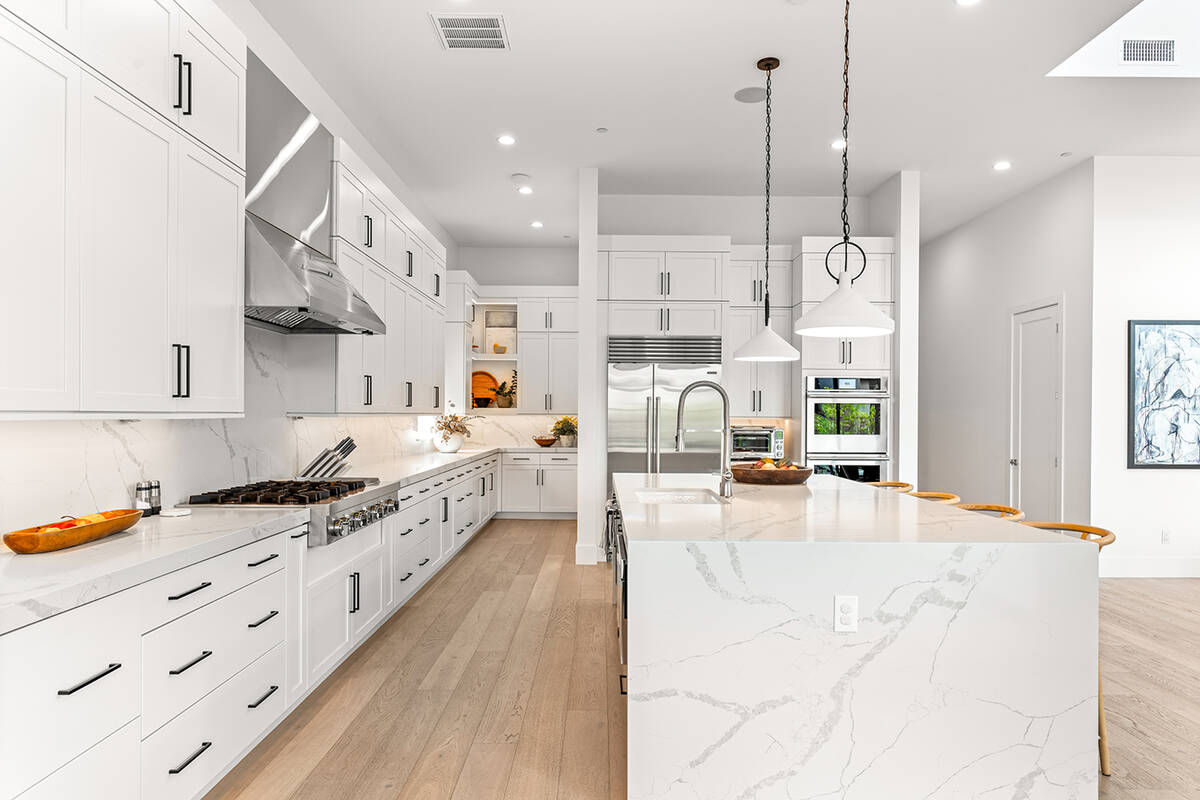 The custom kitchen features an arrangement of built-in white cabinetry adorned with polished ac ...