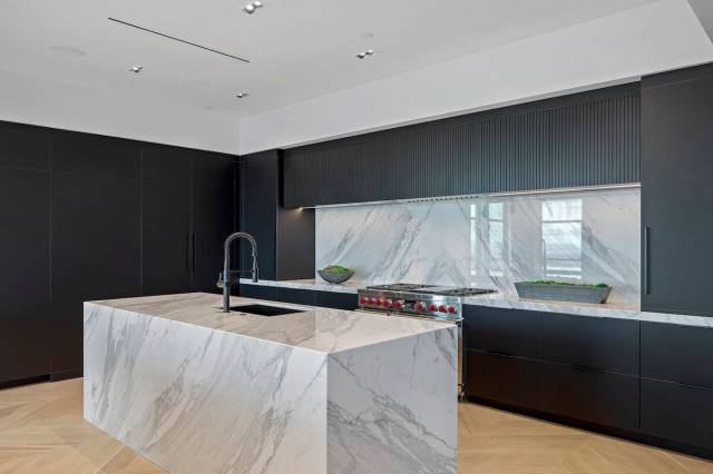 The sleek modern kitchen features dual white-and-gray marble waterfall islands contrasted by bl ...