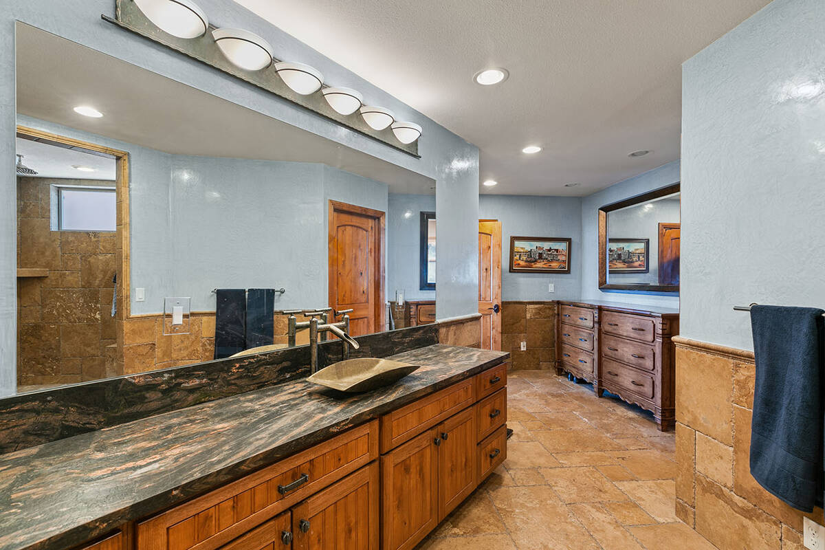 The primary spa-like bath features a voluminous walk-in shower with a stone surround, Venetian ...